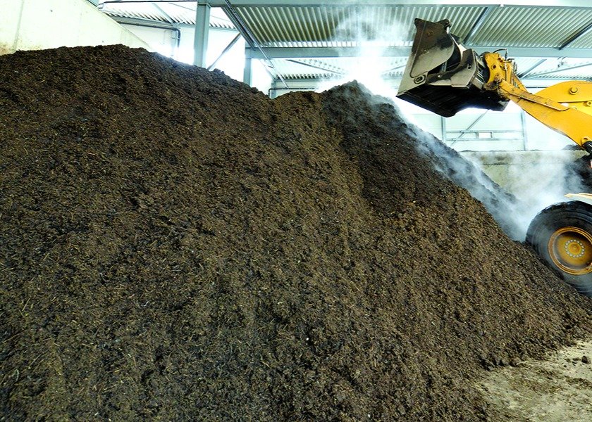 Pile of steaming biosolids being dumped by tractor