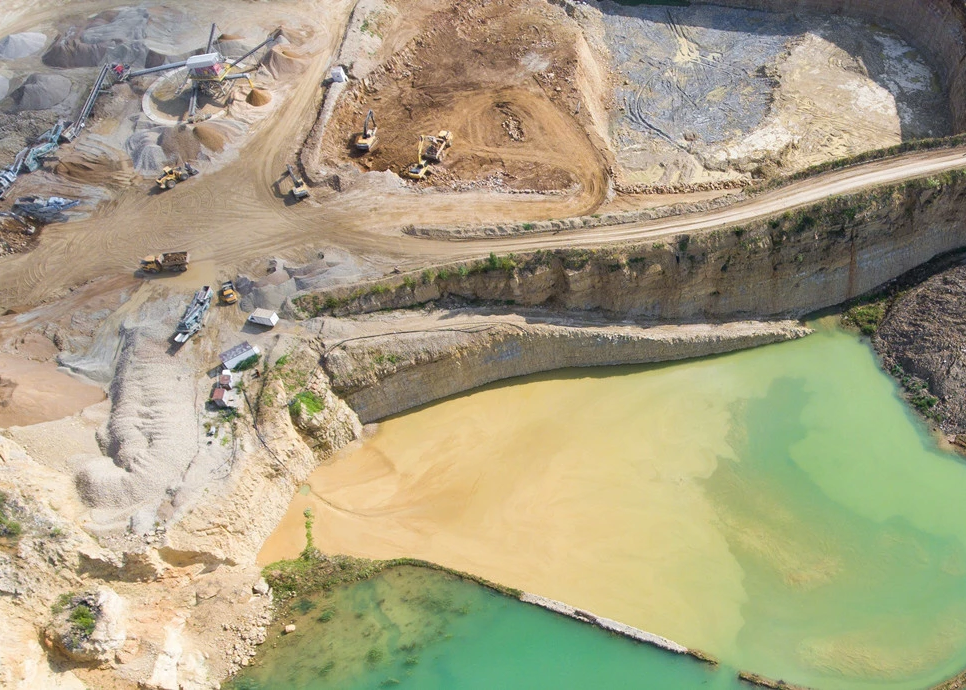 Aerial view of an open-pit mining site with haul roads, excavators, crushers, and stockpiles surrounding a yellow and green tailings pond, illustrating a mine environment suited to flash dryer for mining tailings dewatering solutions.